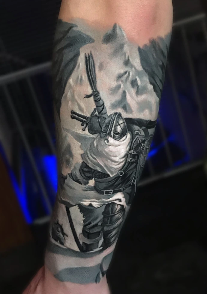 Dieses detailreiche Black-and-Grey Realismus-Tattoo am Unterarm zeigt eine imposante Krieger-Figur in mittelalterlicher Rüstung vor einer schneebedeckten Bergkulisse. Die meisterhafte Umsetzung im Realismus-Stil besticht durch die präzise Darstellung unterschiedlicher Texturen – vom metallischen Glanz des Helms bis zu den weichen Falten des Umhangs –, was dem gesamten Motiv auf engem Raum eine außergewöhnliche Tiefe und erzählerische Dynamik verleiht.