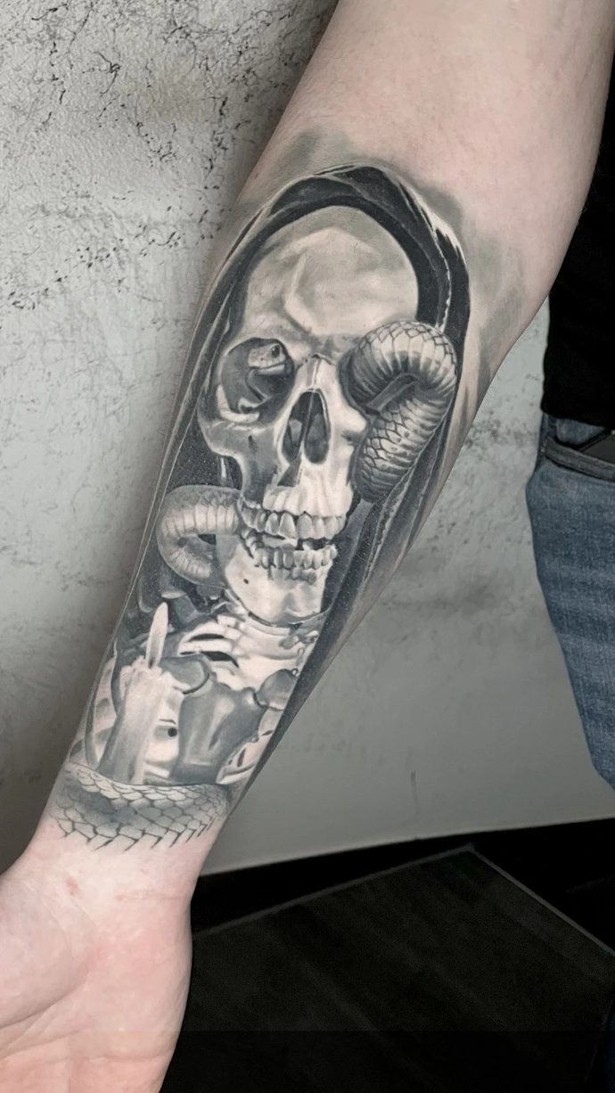 Dieses beeindruckende Black-and-Grey Realismus-Tattoo am Unterarm zeigt eine düstere Komposition aus einem detailreichen Totenkopf und einer sich hindurchwindenden Schlange. Die meisterhafte Umsetzung im Dark-Art-Stil besticht durch die präzise Ausarbeitung der Knochenstruktur und der Schuppentextur, während die tiefen Kontraste und weichen Schattierungen dem Motiv eine außergewöhnliche plastische Tiefe und eine mystische Ausstrahlung auf der Haut verleihen.